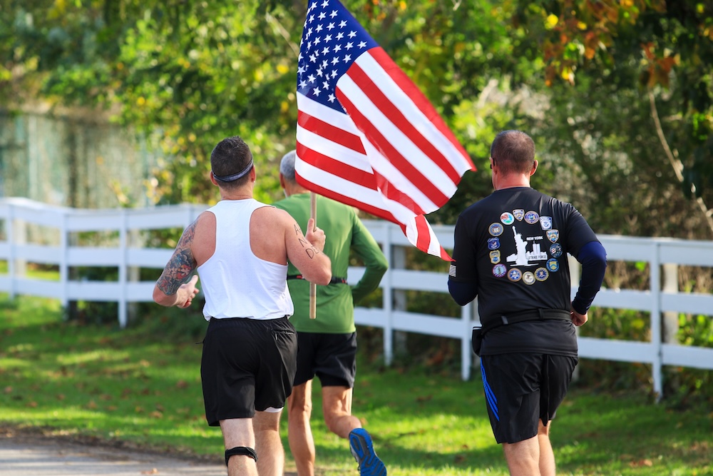 Three men jogging in a race, one is carrying an American flag.